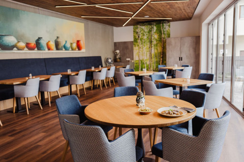 Restaurant mit Holztischen, blauen und grauen Sesseln und einem Wandgemälde