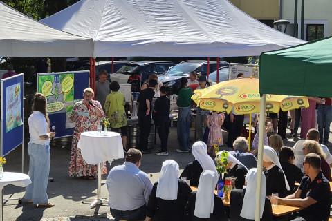 Frau mit Mikrofon spricht bei Veranstaltung in Österreich, Nonnen und Besucher im Hintergrund.