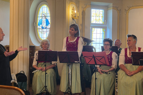 Musikerinnen in Tracht mit Instrumenten, eine ältere Dame gestikuliert.
